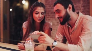 Söz ve barda oturan içecek içme smartphone ile mutlu genç çift. Arkadaşlar hücre kullanarak telefon smartphone birlikte gülümseyen ve bir tarihte gülüyor