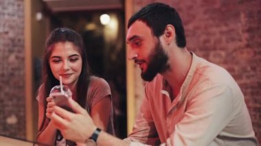 Güzel genç çift Smartphone itting barda kullanarak. Onlar kumar bir spor bahis kazanmak vermek beş kazanmak