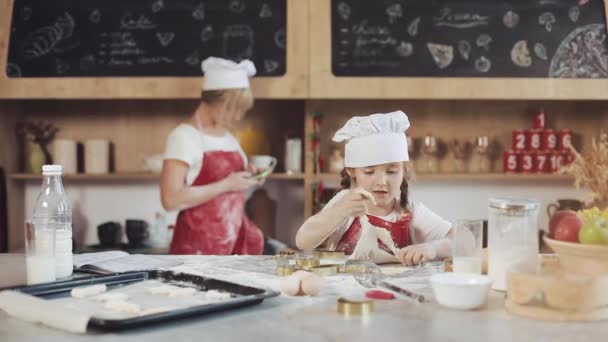 Närbild av liten flicka ha roligt samtidigt som en dotter för cookies i kök rum. Porträtt skott. Inomhus — Stockvideo