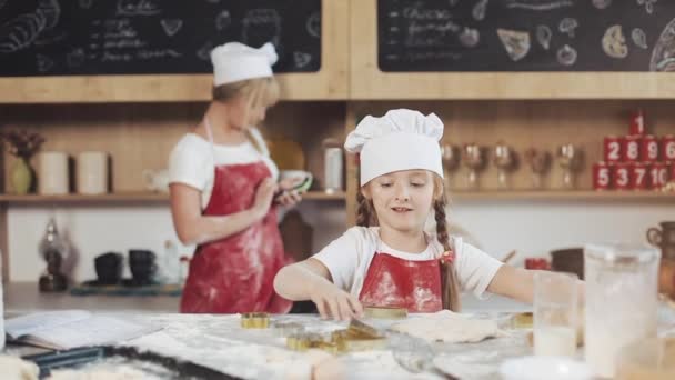 Kleines nettes Mädchen kocht in der gemütlichen Küche. Spaß beim Kuchen- und Plätzchenbacken. Ihre Mutter ist im Hintergrund — Stockvideo