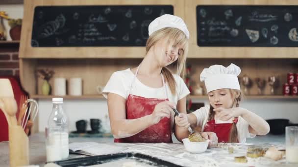 Máma a dcera v stejné oblečení bavit se připravuje těsto na útulné kuchyně. Oni míchání vejce v míse na kitchenl. Vaření, Maminka a dcera koncepce — Stock video