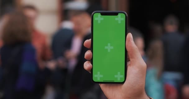 Detailní záběr mans ruky držící mobilní telefon s vertikální zelenou obrazovkou na ulicích — Stock video