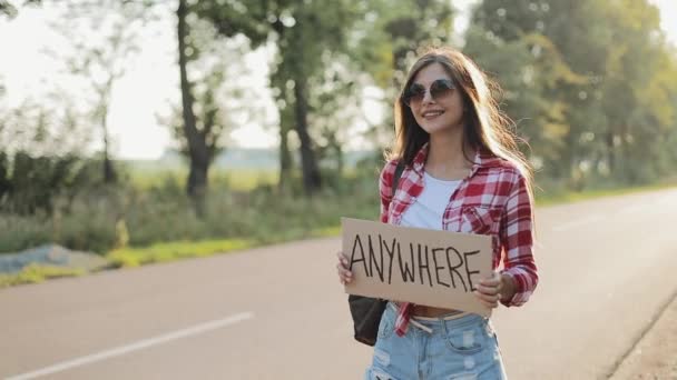 Молода красива жінка автостопом стоїть на дорозі, тримаючи будь-який знак. Літній час — стокове відео