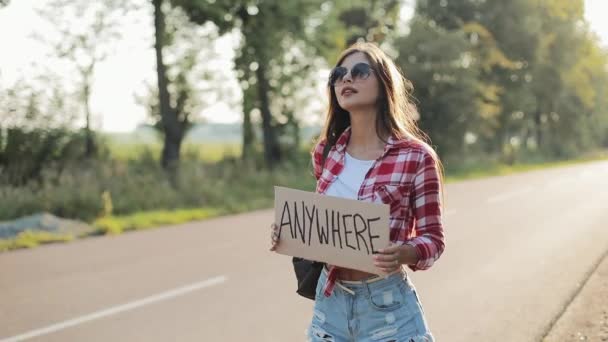 Young beautiful woman hitchhiking standing on the road holding anywhere sign. Summer time — Stock Video