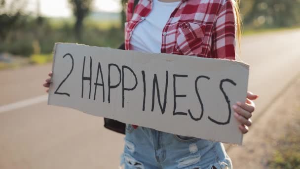 Νεαρή όμορφη γυναίκα ωτοστόπ στέκεται στο δρόμο κρατώντας 2 σημάδι ευτυχίας. Θερινή ώρα — Αρχείο Βίντεο