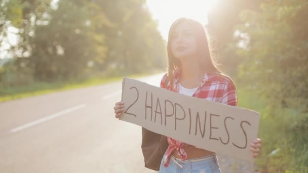 Young beautiful woman hitchhiking standing on the road holding 2 happiness sign. Summer time — Stock Video