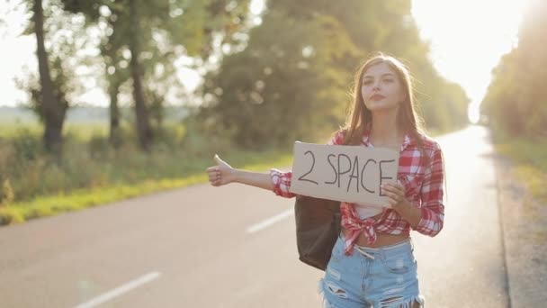 Young beautiful woman hitchhiking standing on the road holding 2 space sign. Summer time — Stock Video