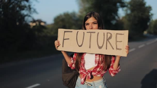 Mulher bonita jovem carona em pé na estrada segurando sinal futuro. Hora de verão — Vídeo de Stock