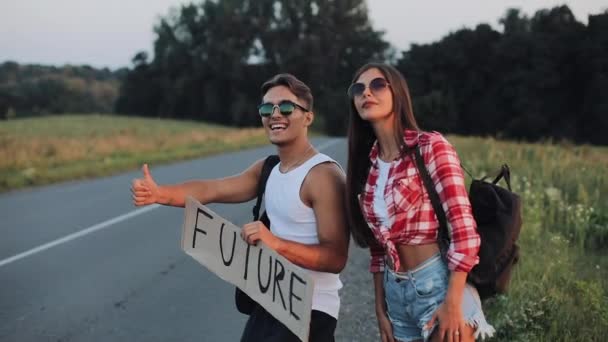 若いカップルが道でヒッチハイクしている立っています。男と女は、記号未来高速道路に車を止めます。ヒッチハイク。旅行者。交通 — ストック動画