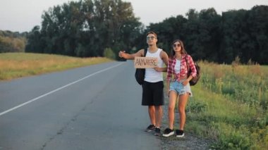 Yolda otostop ayakta olan genç bir çift. Bir erkek ve bir kadın her yerde bir işareti ile karayolu üzerinde durdur