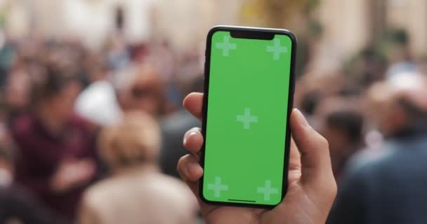 Tembakan jarak dekat dari tangan pria yang memegang ponsel pintar dengan layar hijau di latar belakang jalanan kota. Kunci kroma — Stok Video