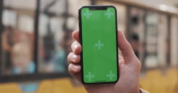 Closeup ενός επανδρώνει το χέρι που κρατά ένα κινητό τηλέφωνο με μια κάθετη πράσινη οθόνη στους δρόμους. Τουριστικό τραμ περνά στο παρασκήνιο — Αρχείο Βίντεο