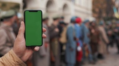 Closeup bir el bir cep telefonu dikey yeşil bir ekran ile sokaklarda tutarak mans. Büyük ekran. Arka planda askeri asker