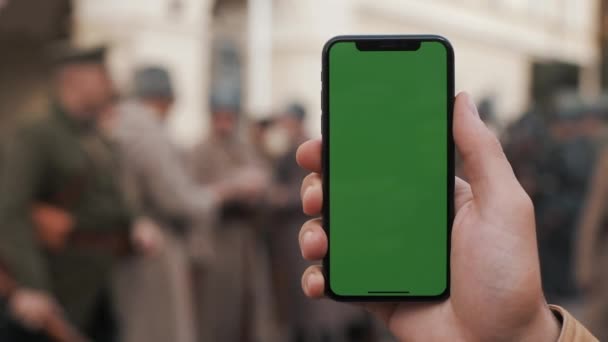 Close-up van een mans bedrijf van de hand en met behulp van mobiele telefoon met een scherm dat verticaal groen op de straten. Militaire soldaten op de achtergrond — Stockvideo