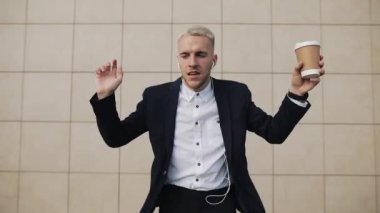 Mutlu genç işadamı kulaklık smartphone ve komik Ofis Binası yakınındaki dans müzik dinlerken kahve ile. Komik dans hamle. Ağır çekim