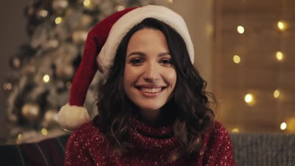 Portret van Smilling aantrekkelijke vrouw in KERSTMUTS kijken naar de Camera op de achtergrond van de kerstboom. Slow motion — Stockvideo