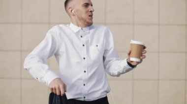 Mutlu genç işadamı kulaklık smartphone ve komik Ofis Binası yakınındaki dans müzik dinlerken kahve ile. Komik dans hamle. Ağır çekim