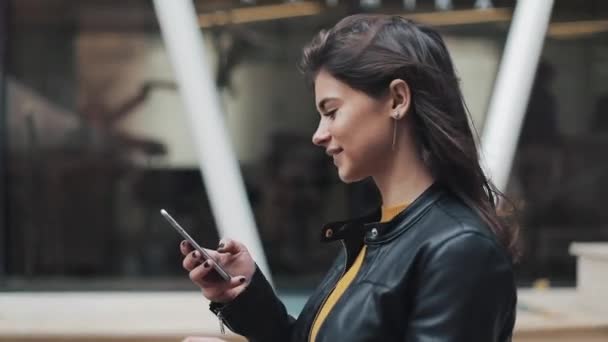 Joven mujer feliz caminando en la calle de la ciudad mientras usa el teléfono inteligente. Movimiento lento — Vídeo de stock