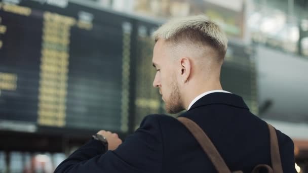 Atraktivní mladý podnikatel čeká nástup na odletové haly na letišti. Dívá se na chytré hodinky — Stock video
