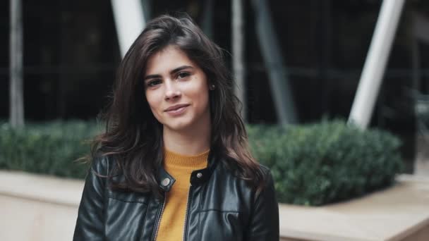 Retrato facial de una atractiva mujer de pie en la calle moderna. Mujer sonriendo. Chaqueta de cuero negro — Vídeo de stock