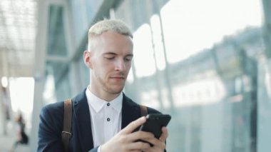 Genç işadamı yakınındaki şehirde yürüyüş Smartphone cep telefonu ile iş app kullanarak. O mesaj gönderdi. Yakışıklı genç işadamı Smartphone emin gülümseyen iletişim