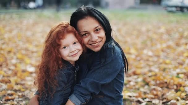 Szczęśliwa matka i jej córka, patrząc na stały aparat w jesienny park. Dziewczyny, uśmiecha się i śmieje się. Zwolnionym tempie — Wideo stockowe