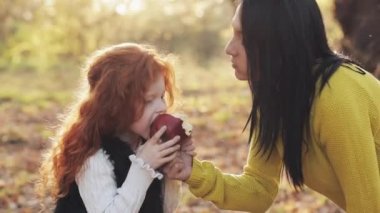 Mutlu bir anne ve birlikte oturan ve bir piknik üzerinde bir şehir parkı içinde elma ile oynarken şirin küçük kız. Sonbahar