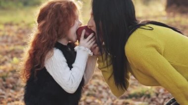 Mutlu bir anne ve birlikte oturan ve bir piknik üzerinde bir şehir parkı içinde elma ile oynarken şirin küçük kız. Sonbahar