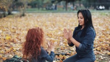 Küçük kızıl saçlı kız onun anne ile sonbahar parkta zaman harcamak. Onlar oynamak ve el çırp