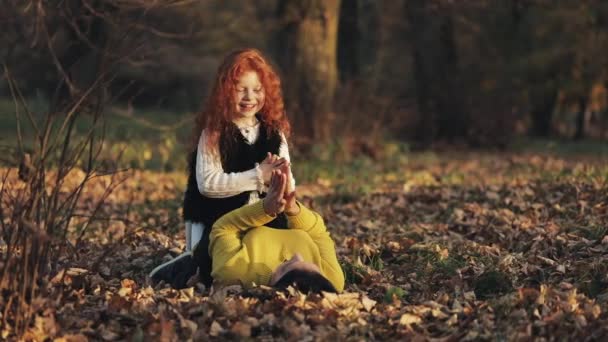 Mamá y su hija juegan. Están jugando con las hojas caídas. Familia feliz en el parque de otoño — Vídeo de stock