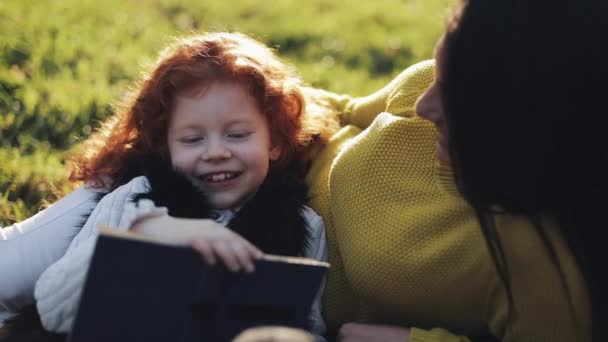 Anya és lánya kis őszi részben ülni és olvasni egy könyvet. Szépen beszélnek. Az őszi erdő boldog család. Lassú mozgás — Stock videók