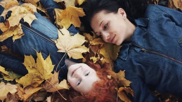 Una hermosa madre y su linda hija yacen sobre una hoja amarilla en el parque de otoño. Mamá besa a su hija. La familia feliz se está divirtiendo. Vista superior, cámara lenta — Vídeos de Stock