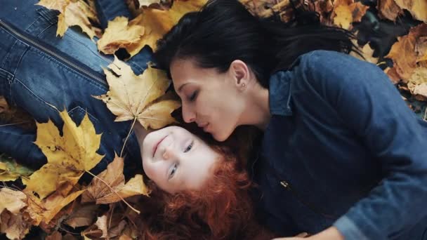 Una hermosa madre y su linda hija yacen sobre una hoja amarilla en el parque de otoño. Mamá besa a su hija. La familia feliz se está divirtiendo. Vista superior, cámara lenta — Vídeo de stock