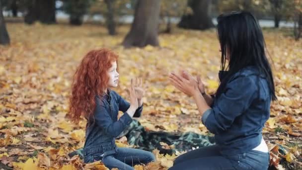 Liten rödhårig flicka med hennes mamma tillbringar tid i höst park. De spelar och klappa händerna — Stockvideo