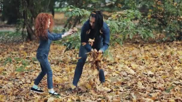 Glückliche Mutter und ihre kleine Tochter haben Spaß im Herbstpark. junge Familie wirft Blätter und lacht. Zeitlupe — Stockvideo