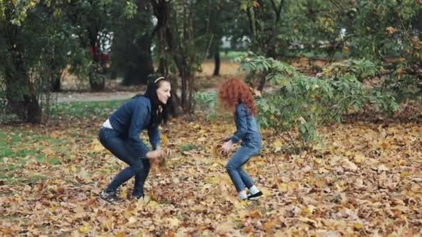 Feliz madre y su hijita divirtiéndose en el parque de otoño. Familia joven lanzando hojas y riendo. En cámara lenta. — Vídeo de stock