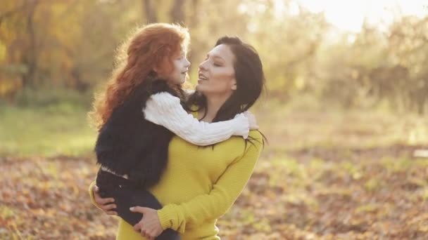 Güzel bir anne ve tatlı kızı sonbahar parkta yürüyorlar. Anne holdeng kızı kucağında. Onlar gülüyor, konuşmak ve iyi eğlenceler — Stok video