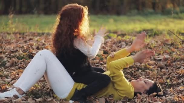 Mamá y su hija juegan. Están jugando con las hojas caídas. Familia feliz en el parque de otoño — Vídeos de Stock