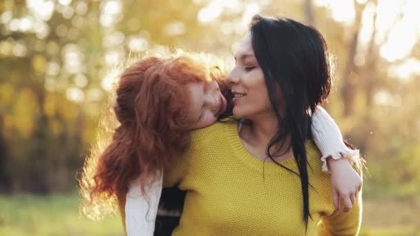 Feliz joven madre y su pequeña hija pelirroja divirtiéndose en un parque de otoño. Juegan, se abrazan y ríen. Movimiento lento — Vídeos de Stock