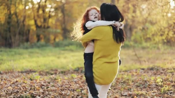 Feliz joven madre y su pequeña hija pelirroja divirtiéndose en un parque de otoño. Juegan, se abrazan y ríen. Movimiento lento — Vídeo de stock