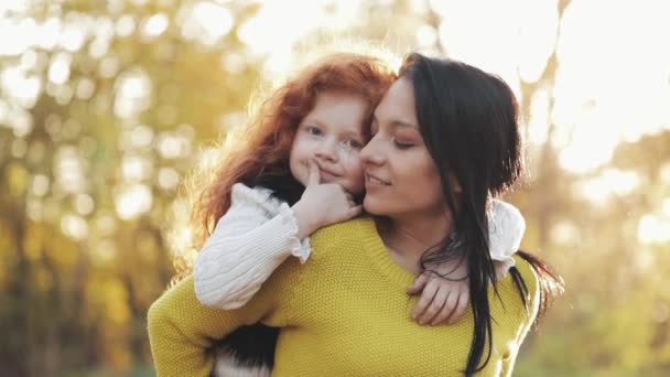 Счастливая молодая мама и ее рыжая дочь веселятся в осеннем парке. Они играют, обнимаются и смеются. Медленное движение — стоковое видео