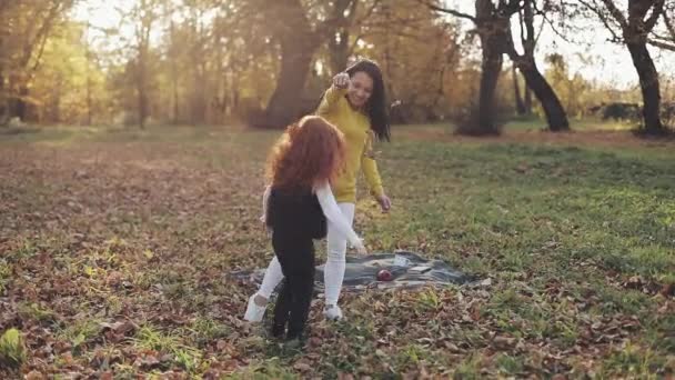 Счастливая молодая мама и ее рыжая дочь веселятся в осеннем парке. Они играют, бросают листья и смеются. Медленное движение — стоковое видео