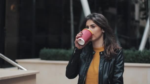 Молодая красивая женщина пьет кофе и ходит по улице рядом с бизнес-центром — стоковое видео