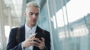Genç çekici işadamı kahve tutarak ve telefon kullanarak sokakta yürüyor