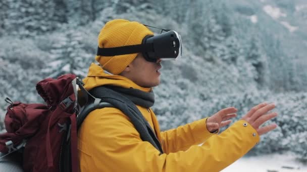 Молодой привлекательный мужчина в жёлтой куртке наслаждается очками виртуальной реальности или 3D-игрой на свежем воздухе в зимних горах. Технологии, инновации, киберпространство и азартные игры — стоковое видео