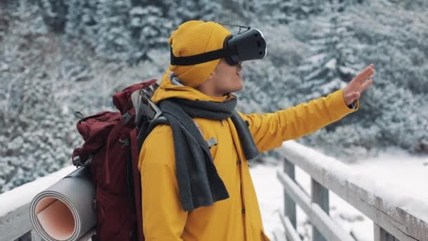 Joven hombre atractivo en chaqueta amarilla disfrutando de gafas de realidad virtual auriculares o 3d juego al aire libre en las montañas de invierno. Tecnología, innovación, ciberespacio y juegos — Vídeo de stock