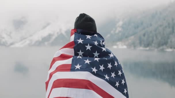 美しい湖の近く雪に覆われた山の中のアメリカの地位のフラグと旅行者の男。美しい自然を見てハイカー — ストック動画