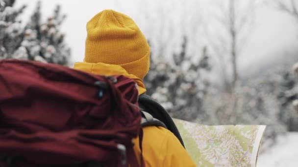 산에 여행. 숲에서 산책 지도 들고 노란색 겨울 옷을 입고 젊은 사람이 눈으로 덮여. 뒤에서 보기 여행, 모험, 등산 — 비디오