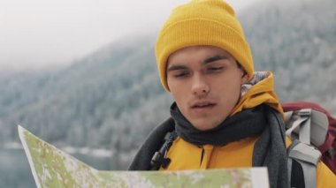 Dağlarda seyahat. Genç uzun yürüyüşe çıkan kimse bir kağıt harita alanı kullanır. Yolunu arar. Macera ve seyahat hoşlanıyor. Bir arka plan kış dağlar ve güzel bir göl üzerinde
