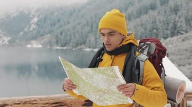 Dağlarda seyahat. Genç uzun yürüyüşe çıkan kimse bir kağıt harita alanı kullanır. Yolunu arar. Macera ve seyahat hoşlanıyor. Bir arka plan kış dağlar ve güzel bir göl üzerinde